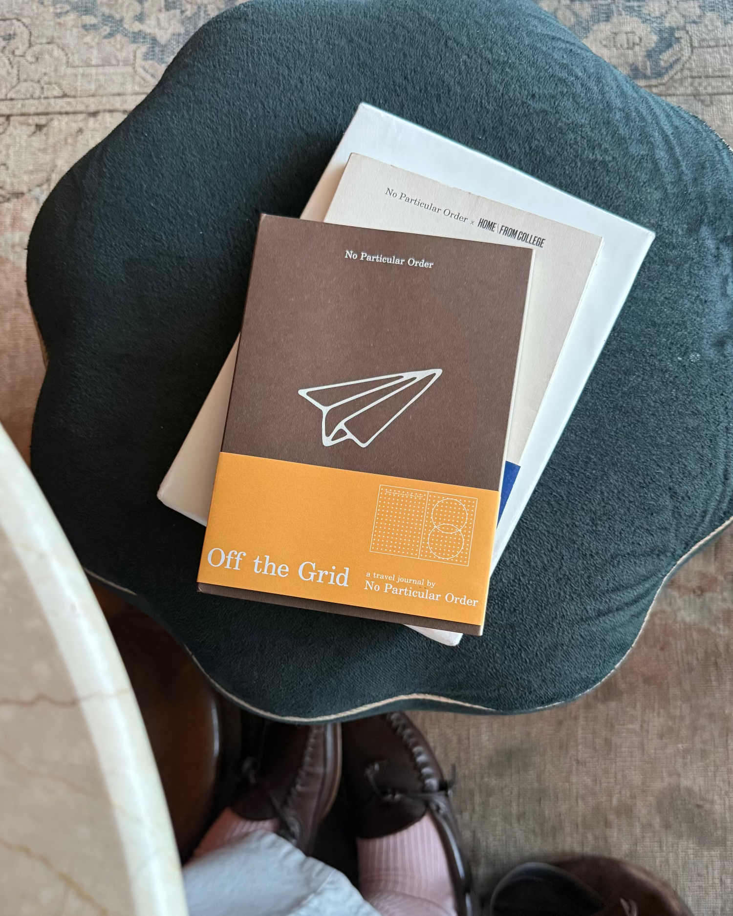 Stack of books on a cushion with a person sitting on the floor.